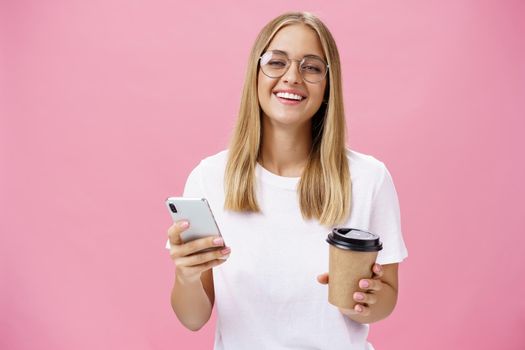 Busy freelancer sipping coffee and working via smartphone talking to clients while sitting in cafe or coworking place, laughing joyfully at camera with broad smile holding paper cup and cellphone. Van life, lifestyle, technology and digital nomad concept