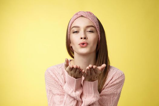 Happy valentines day. Charming romantic and sensual young flirty woman in knitted headband, sweater extending palms near folded lips sending air mwah, blowing kiss tender and gentle.