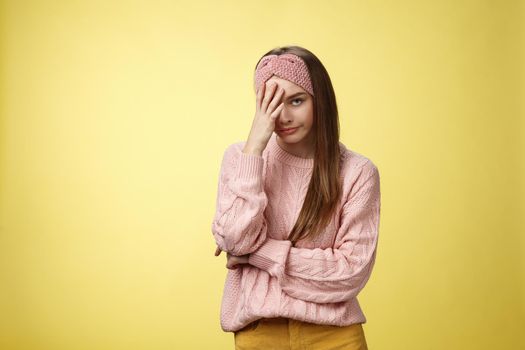 Woman facepalming covering face annoyed, bothered and inrritated, smirking looking with dismay, pissed off, posing unhappy displeased, staring indignant and upset posing tired over yellow background.