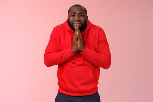 Miserable african american man beard in red hoodie stooping make supplicating upset grimace grying sobbing asking help say please hold hands pray begging mercy, apologizing need money.