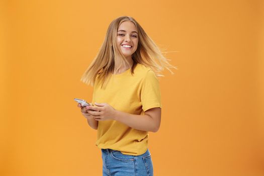 Girl feeling happy receiving message from him. Portrait of carefree charming woman with new haircut waving head standing half-turned, turning to camera with pleased cute smile holding smartphone. Emotions and technology concept