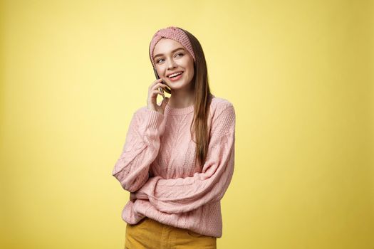 Talkative attractive glamour young 20s european woman wearing sweater, knitted headband tilting head looking away smiling curious, enjoying pleasant conversation via smartphone, talking to friend.