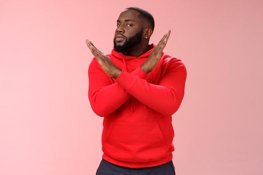 Cut it out. Portrait serious-looking african american male assisant show cross gesture say finish refusing, rejecting offer never gonna do it, standing reluctant pink background negative answer.