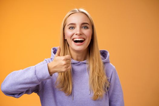Supportive happy glad young blond attractive woman in hoodie adore perfect good idea show thumbs up approval like gesture smiling broadly accept interesting concept recommend, satisfied.