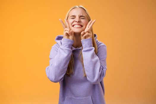 Excited lucky charming friendly blond girlfriend having fun celebrating perfect news best score receive scholarship smiling amused carefree close eyes show peace victory signs, orange background.