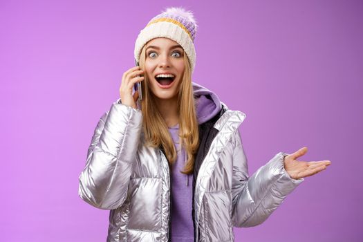 Talkative amused blond girl hearing awesome good news raise hand surprised glad talking smartphone widen eyes satisfied perfect information, standing astonished pleased purple background.