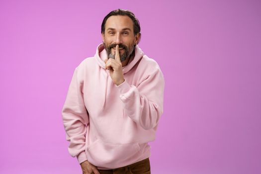 Lips sealed secret. Portrait alluring cheeky stylish adult bearded guy in pink hoodie asking keep quiet show shush shh gesture index finger pressed mouth smiling devious smug face, have idea.