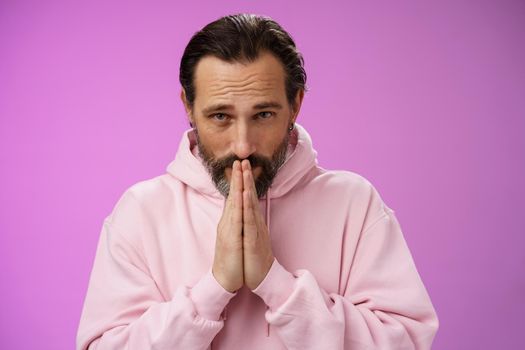 Worried intense serious-looking troubled handsome mature bearded man praying waiting important news nervously looking camera press palms supplicating wish wife alright, standing purple background.