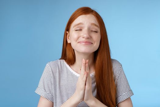 Girl making wish bottom heart willing dream come true press palms together pray supplicating close eyes smiling sincere belief desire fulfill anticipating miracle, standing blue background.