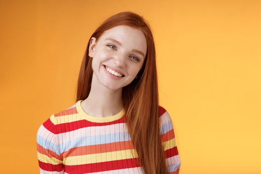 Pleasant charismatic young confident carefree redhead charming girl tilting head smiling broadly white teeth talking casually good mood express positive happy emotions standing orange background.