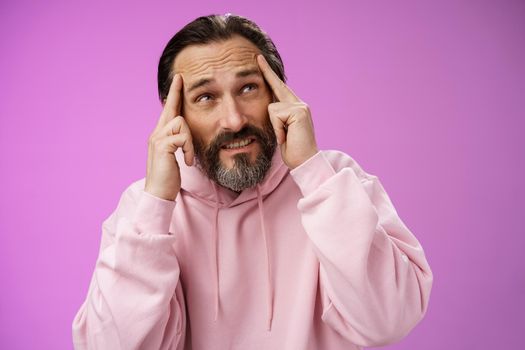 Worried intense disturbed mature male writer cannot create idea standing pressured touch forehead frowning look up problem concentrate not focused, standing purple background upset distracted.