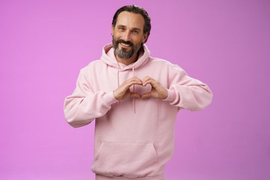 Family in heart. Portrait lovely handsome romantic bearded man in pink hoodie passionatly looking camera show love gesture smiling cute expressing romantic sympathy attitidue, purple background.
