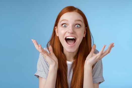 Lifestyle. Excited overwhelmed young attractive female redhead fan go nuts thrilled wide eyes surprised yelling astonished receive exciting good news raise hands triumphing winning lottery extremely happy.