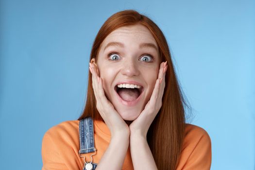 Impressed excited overwhelmed young redhead girlfriend fan screaming thrilled express afection adore awesome music band yelling happily reacting surprised astonished, standing blue background.