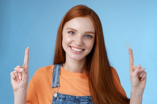 Waist-up charismatic good-looking european redhead woman smiling sincere gladly showing way pointing up index fingers happy help recommend cool advertisement spot, blue background.