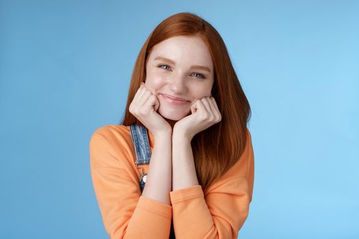 Tenderness, wellbeing, beauty conept. Attractive young ginger girl pure skin blue eyes lean palms silly smiling camera look amused enthusiastic listen interesting stories gladly, blue background.