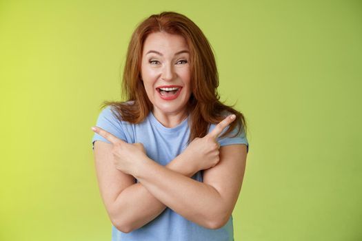 Lifestyle Concept - Happy carefree entushiastic redhead funny mature female. having fun positive attitude cross arms body pointing sideways show left right products laughing happily like both choices green background.