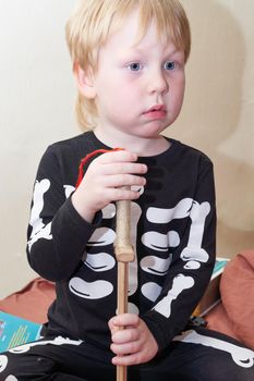 A child in a skeleton costume with a wooden sword sits on the couch. Children games, fears and horror stories