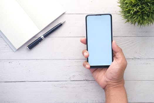 Top view of man hand holding smart phone with empty screen on office desk .