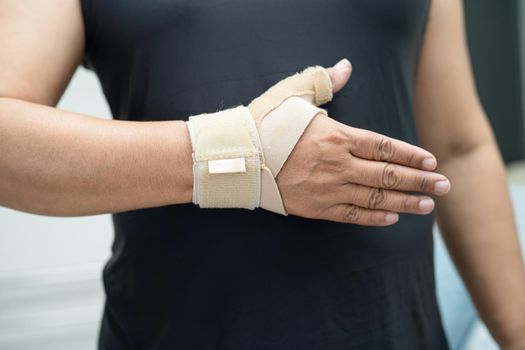 Asian middle-aged lady woman use elastic bandage to treating De Quervain syndrome at hand and finger in office.