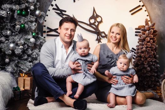 A happy big family with twin children in the New Year's interior of the house against the background of a large clock.