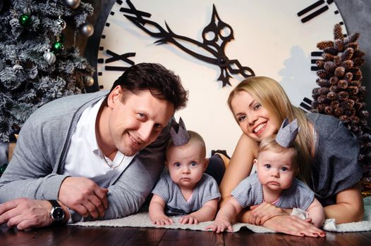 A happy big family with twin children in the New Year's interior of the house against the background of a large clock.