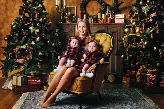 A happy mother with her twin children in the New Year's interior of the house on the background of a Christmas tree.