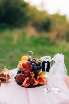 A painted table with a bookcase with fruits and glasses for champagne in the suits of the bride and groom. High quality photo