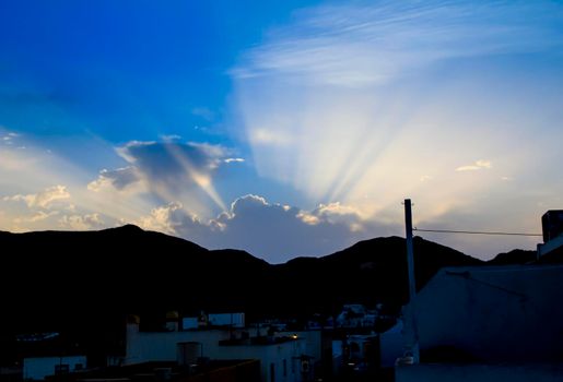 Sunbeam shining trough cloudy sky before sunset to mountain range
