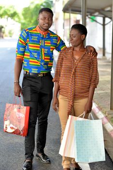 young woman standing in brown pants with bag in hand looking in profile while the man looks at the camera smiling.