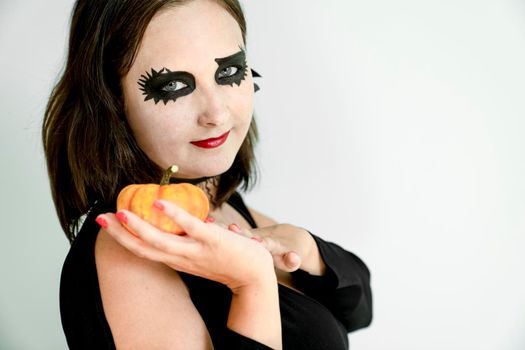 Woman with Halloween makeup on face holds pumpkin in hand on gray background close-up portrait.