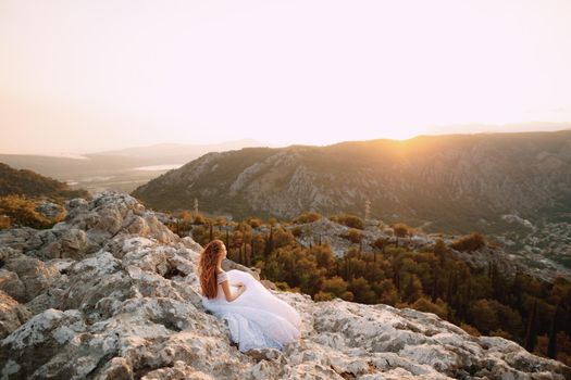 The bride in tender wedding dress sits on the rock on Mount Lovcen and looks at the Bay of Kotor . High quality photo