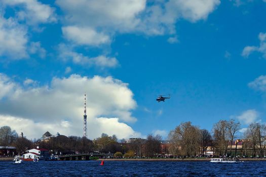 The helicopter takes off against the background of clouds and blue sky next to the TV tower. Small aircraft for excursions