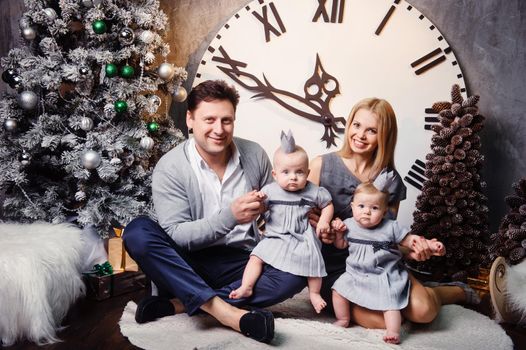 A happy big family with twin children in the New Year's interior of the house against the background of a large clock.