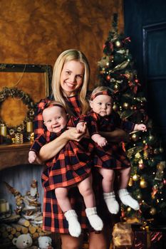 A happy mother with her twin children in the New Year's interior of the house on the background of a Christmas tree.
