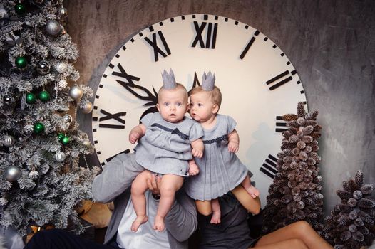 A happy big family with twin children in the New Year's interior of the house against the background of a large clock.