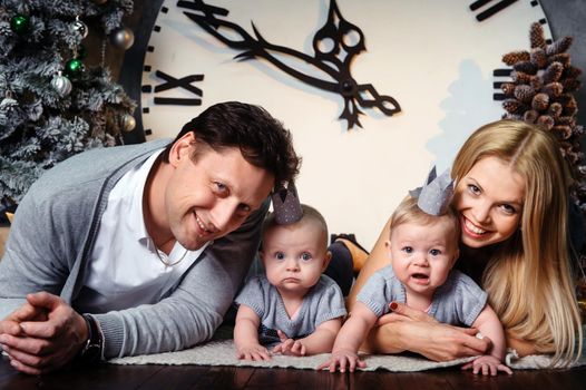 A happy big family with twin children in the New Year's interior of the house against the background of a large clock.