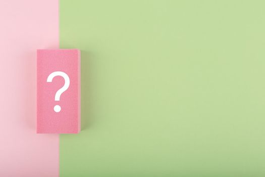 White question mark on colored pink and green background with copy space. Flat lay, trendy minimal composition with question