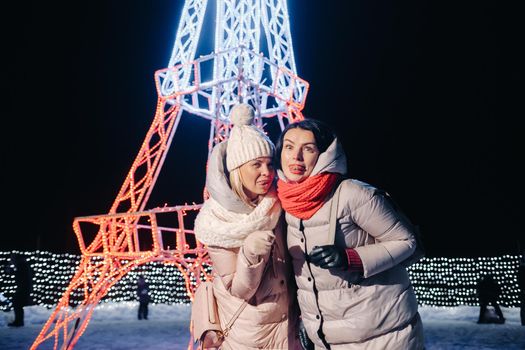 two girls in winter with New Year's eve lights burning on Christmas street.