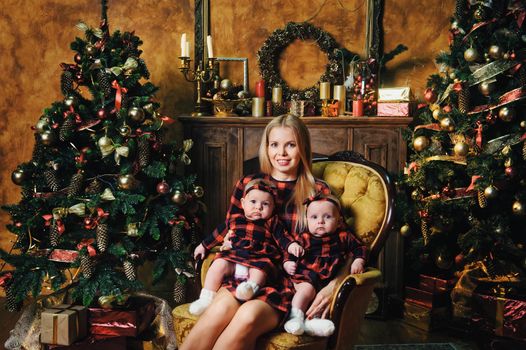 A happy mother with her twin children in the New Year's interior of the house on the background of a Christmas tree.