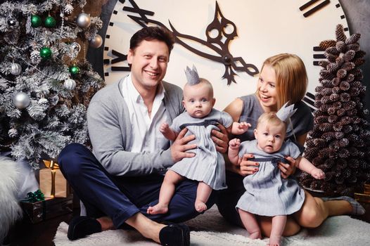 A happy big family with twin children in the New Year's interior of the house against the background of a large clock.