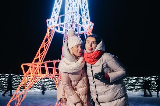 two girls in winter with New Year's eve lights burning on Christmas street.