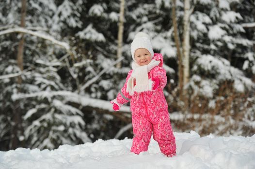 a little girl in a pink suit walks outside in winter.