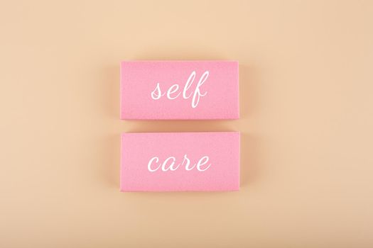 Self care, mental health, self love and acceptance concept. Hand written text on pink tablets against beige background. Trendy minimal composition