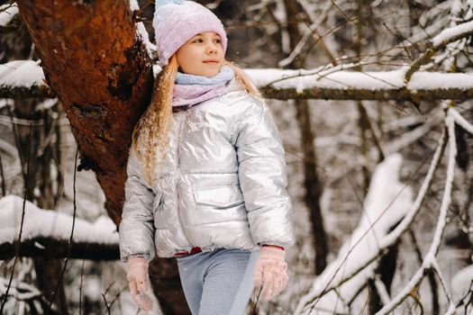 a little girl in a silver jacket in winter goes outside in winter.