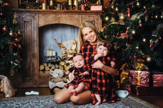 A happy mother with her twin children in the New Year's interior of the house on the background of a Christmas tree.