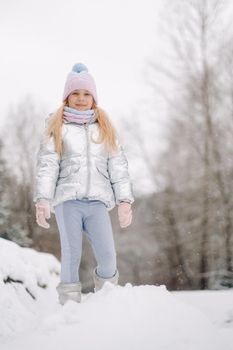 a little girl in a silver jacket in winter goes outside in winter.