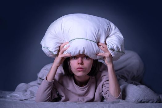 Young girl holds a pillow and hid under a blanket from all problems, procrastinating, millennials generation. Sad woman is worried about insomnia, poor sleep, getting stress.