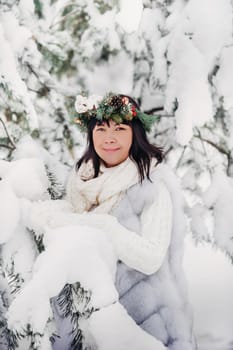 Portrait of a woman in white clothes in a cold winter forest. Girl with a wreath on her head in a snow-covered winter forest