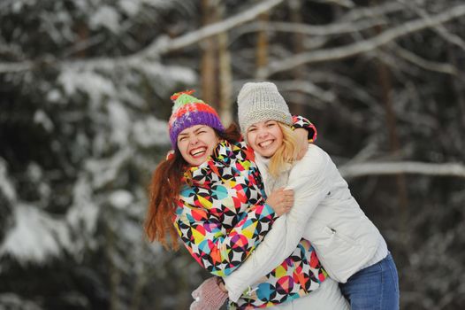 Two girls in the winter forest emotionally hug and smile.Happy women hug and Express joy.